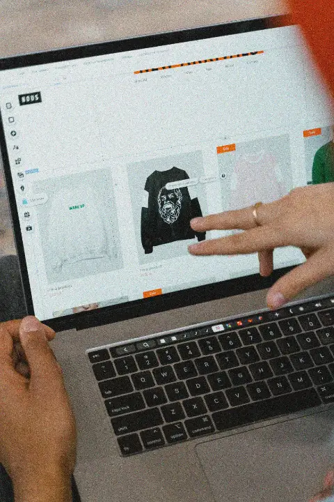 Two people at a laptop, one pointing at a product in an online shop's editor.